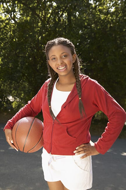 A young athlete in a red sweatshirt poses for a photo with her basketball, her braces clearly visible in her smile.