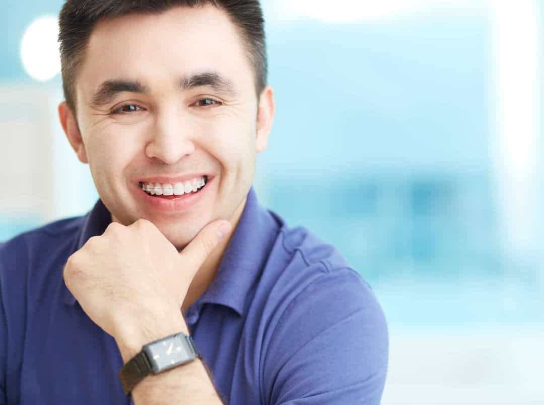 A cheerful man with adult braces and a purple shirt smiles.