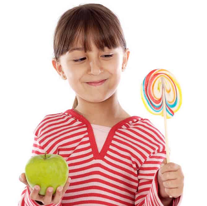 A young girl holds an apple in one hand and huge lollipop in the other, struggling to decide which to eat.